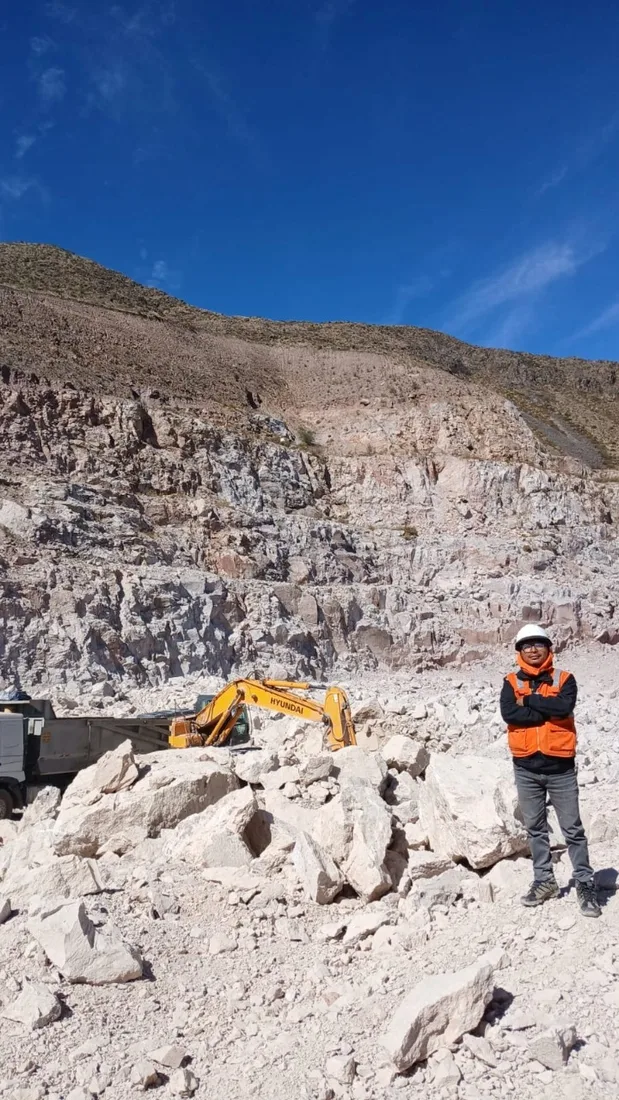 Ingeniero de WASI con casco y chaleco en una cantera, junto a una excavadora